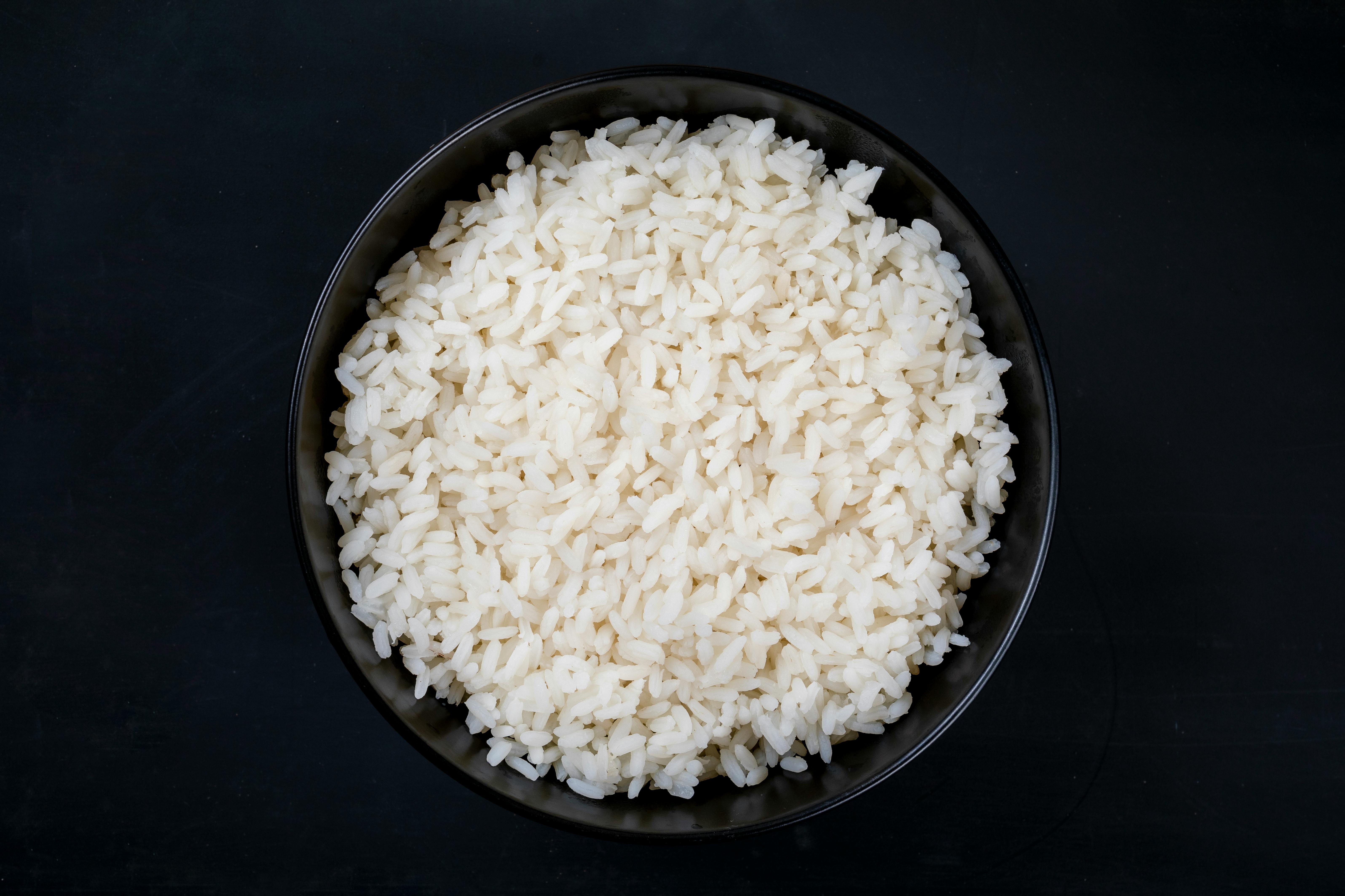 A bowl filled with freshly cooked white rice, shot from above against a dark background for contrast.